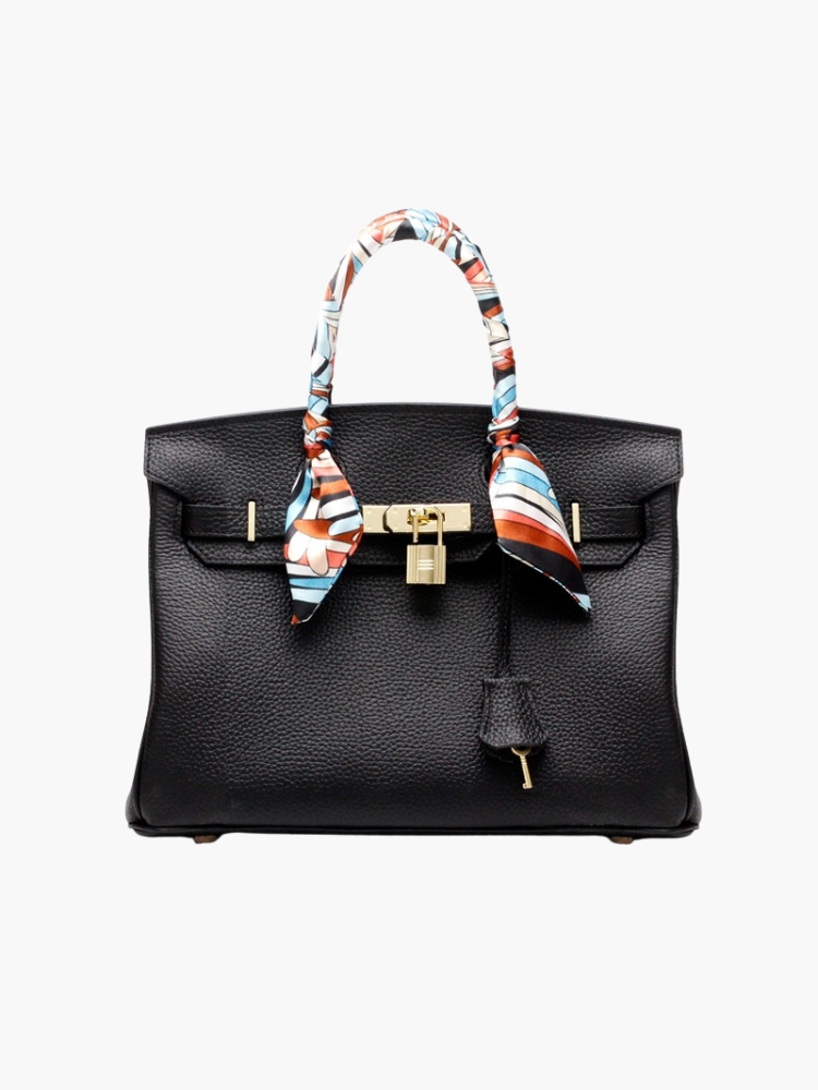 Black structured handbag with gold lock and colorful scarf-wrapped handles