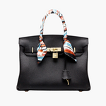 Black structured handbag with gold lock and colorful scarf-wrapped handles