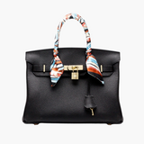 Black structured handbag with gold lock and colorful scarf-wrapped handles
