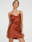 Woman wearing dark rust satin mini slip dress with cowl neckline and spaghetti straps