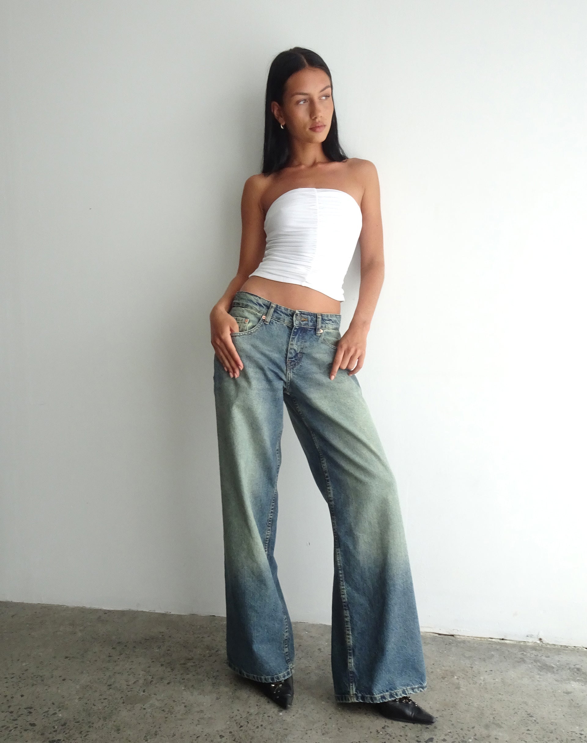 Woman wearing oversized low-rise wide leg jeans in extreme blue green with a white tube top