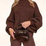 Woman wearing a chunky brown knit sweater and holding a dark brown croc-embossed mini handbag with gold hardware