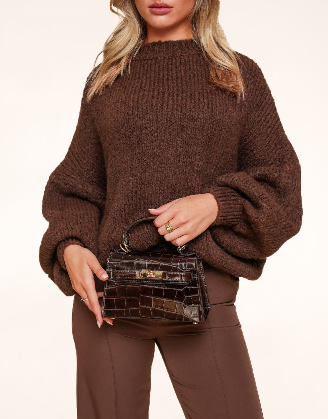 Woman wearing a chunky brown knit sweater and holding a dark brown croc-embossed mini handbag with gold hardware