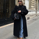 Woman wearing oversized black wool longline coat with jeans and boots, styled for chic winter street fashion