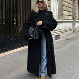 Woman wearing oversized black wool longline coat with jeans and boots, styled for chic winter street fashion