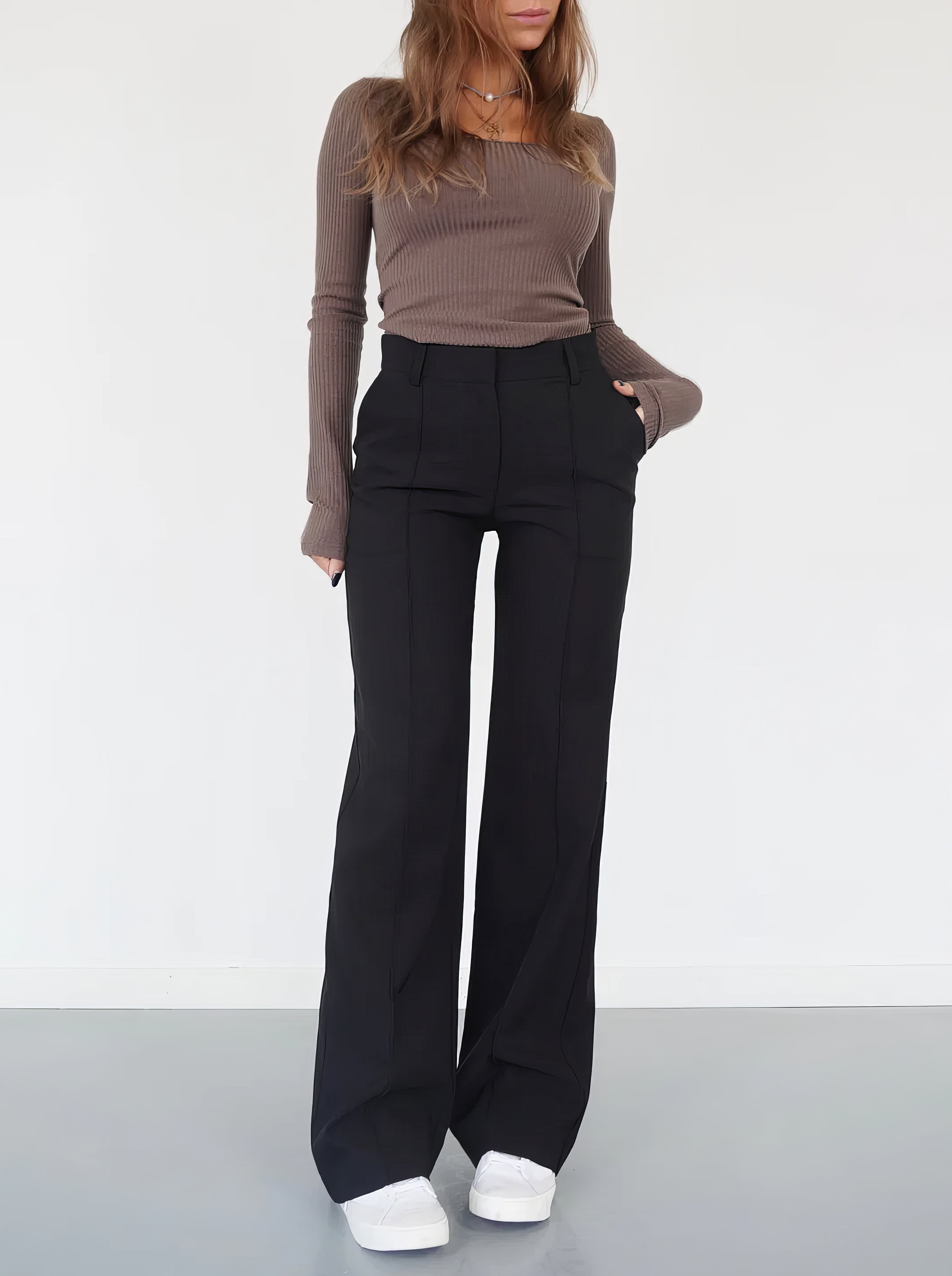 Woman wearing high-waisted black wide-leg trousers with a ribbed brown top and white sneakers